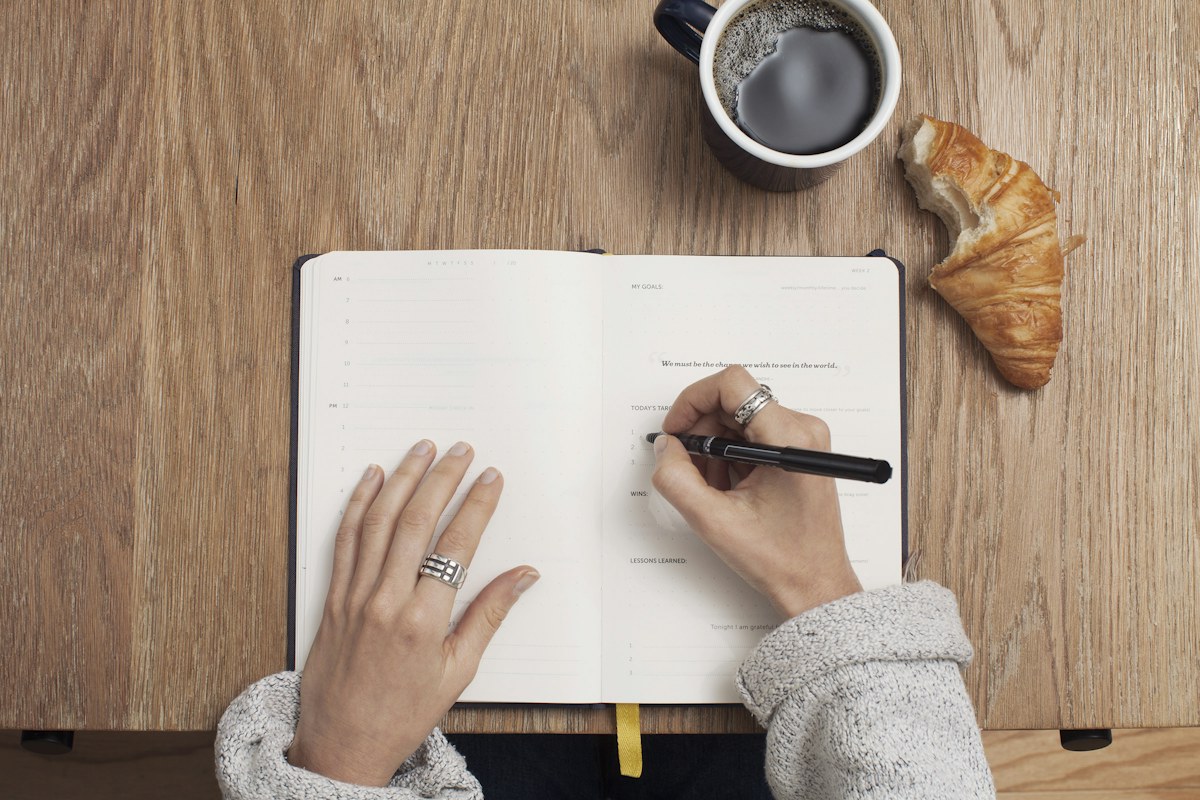 Someone writing in an open planner beside a coffee